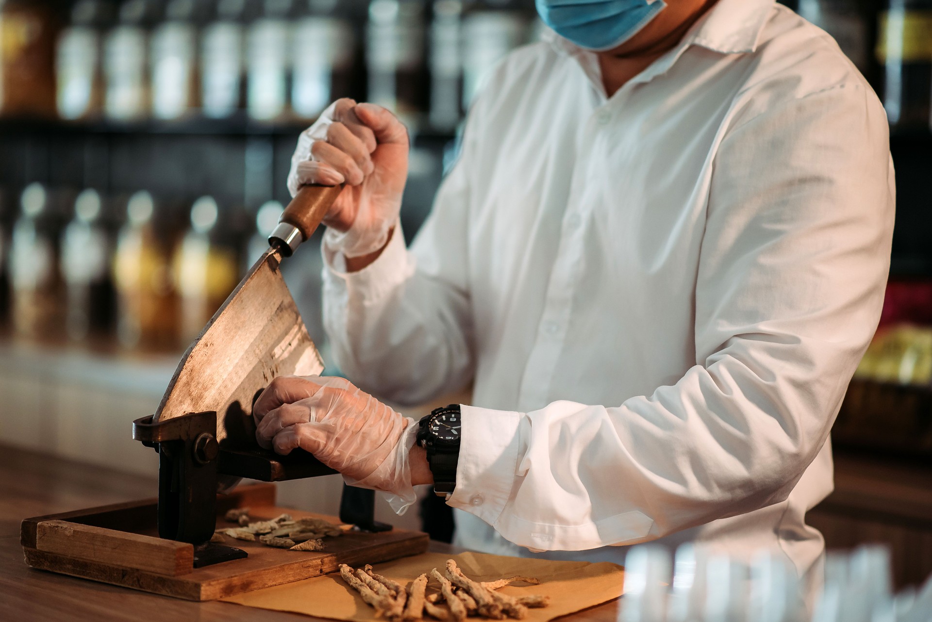 Farmacista maschio cinese asiatico che taglia le erbe cinesi davanti al bancone del negozio di medicina cinese